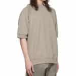 A person wearing an Essentials Taupe Cotton Sweatshirt with matching pants is standing against a plain white background. Their long, wavy hair cascades over their shoulders. The outfit looks casual and comfortable.