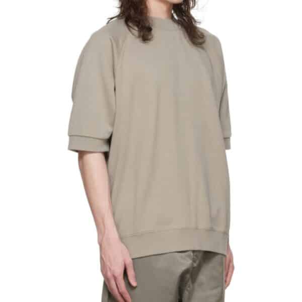 A person wearing an Essentials Taupe Cotton Sweatshirt with matching pants is standing against a plain white background. Their long, wavy hair cascades over their shoulders. The outfit looks casual and comfortable.