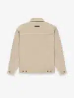 The image displays the back of the Fear of God Taupe Zip Denim Jacket 'Dusty Beige', featuring long sleeves with buttoned cuffs, a straight cut, and a small rectangular patch near the collar on the upper back. The jacket is set against a plain white background.