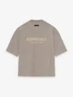 The Fear of God Essentials V-Neck T-Shirt 'Core Heather' features a beige design with the words ESSENTIALS and FEAR OF GOD prominently printed in bold, light-colored letters on the back against a plain backdrop. It boasts a relaxed fit and short sleeves.