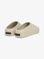 A pair of The California Shoes in beige, featuring a minimalist slip-on design with black labels at the heel, is placed on a white background.