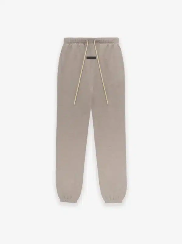 The 'Core-Heather' Fear of God sweatpants, which are tan with a drawstring waistband and elastic cuffs, are displayed against a plain background and showcase subtle branding on the front.