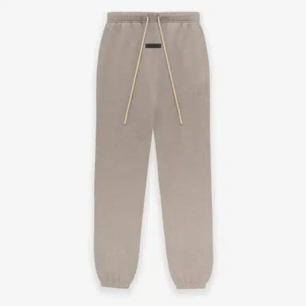 The 'Core-Heather' Fear of God sweatpants, which are tan with a drawstring waistband and elastic cuffs, are displayed against a plain background and showcase subtle branding on the front.