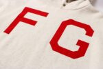 A cream-heather hoodie from Fear of God Essentials with prominent red F and G letters on the front.