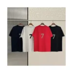 Four Fear of God Essentials 7 T-Shirts are on hangers, featuring red, white, black, and black colors (from left to right), set against a textured background.