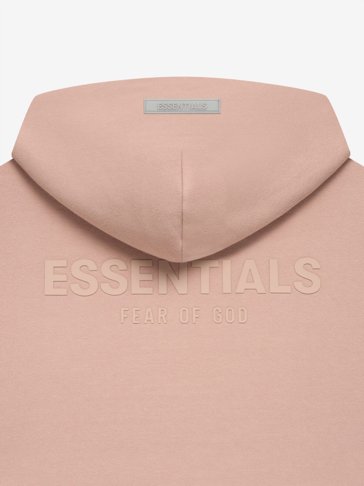 A close-up image showcases the back of a pink Fear of God Essentials Pullover Hoodie. The text "ESSENTIALS" is prominently displayed, with "FEAR OF GOD" written below it. A small tag labeled "ESSENTIALS" is visible at the top of the hood.