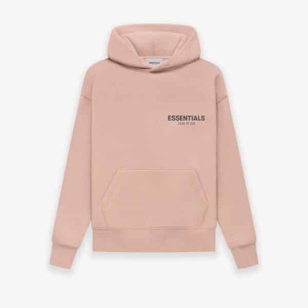 A 'Pink' hoodie from Fear of God Essentials features a front pocket and hood. The chest showcases the text ESSENTIALS Fear of God in black print, set against a plain white background.