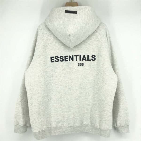 A light gray Essentials Fleeces Thick Hoodie featuring bold black "ESSENTIALS" text on the back with "GOD" in smaller letters beneath, displayed on a hanger against a light background.