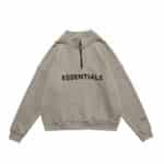 The Essentials Half Zip High Collar Loose Hoodie is a beige sweatshirt featuring a half-zip design, with "ESSENTIALS" printed in black across the chest and on the left sleeve near the wrist. It comes with long sleeves and a high collar.