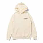 The Fear Of God Essentials Star Hoodie is cream-colored, featuring black "ESSENTIALS" and "FEAR OF GOD" text on the upper left chest. It comes with a front pocket and a hood, showcasing a simple and minimalistic design.