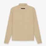 A khaki Fear of God ESSENTIALS Twill Jacket is displayed from the back, showcasing a simple design with a point collar and a small black tag near the neckline. The jacket is laid flat against a plain white background.