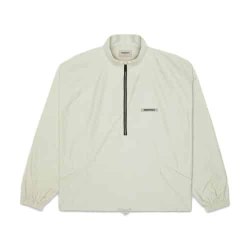 The Fear of God Essentials Half Zip Jacket is a light beige, long-sleeved pullover with a half-zip, elastic cuffs, and a small logo on the chest.