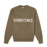 The Fear of God Essentials Knitted Sweater Harvest features a khaki green color with the word "ESSENTIALS" boldly displayed in large white letters across the chest. It includes ribbing on the crew neckline, cuffs, and hem, all set against a plain white background.