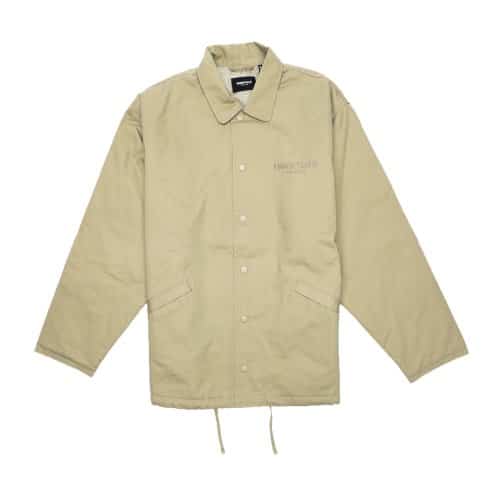 Fear of God Essentials Work Jacket in beige, featuring a button-up design with a collar, a small embroidered logo on the left chest, long sleeves, two front pockets, and a drawstring at the hem.