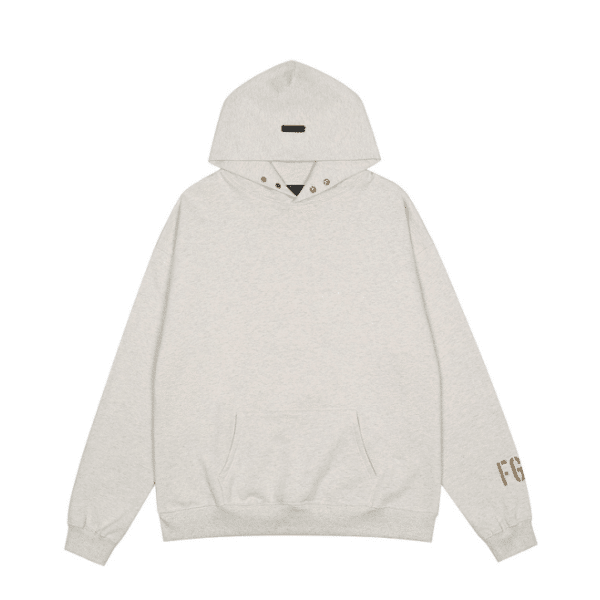 Introducing the Fear of God Essentials FG7C Hoodie in 'Light-Oatmeal': This hoodie boasts a minimalist design, featuring a front pocket and drawstring hood adorned with gold grommets. The left sleeve is subtly detailed with "F.G" in brown letters.